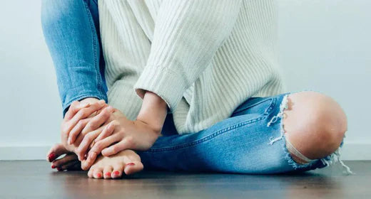 Person sitting on the ground with their hands holding their own foot