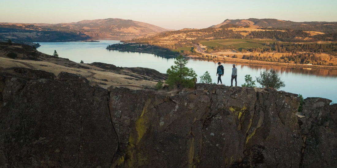 People outdoors hiking on ridge above a riverbank.