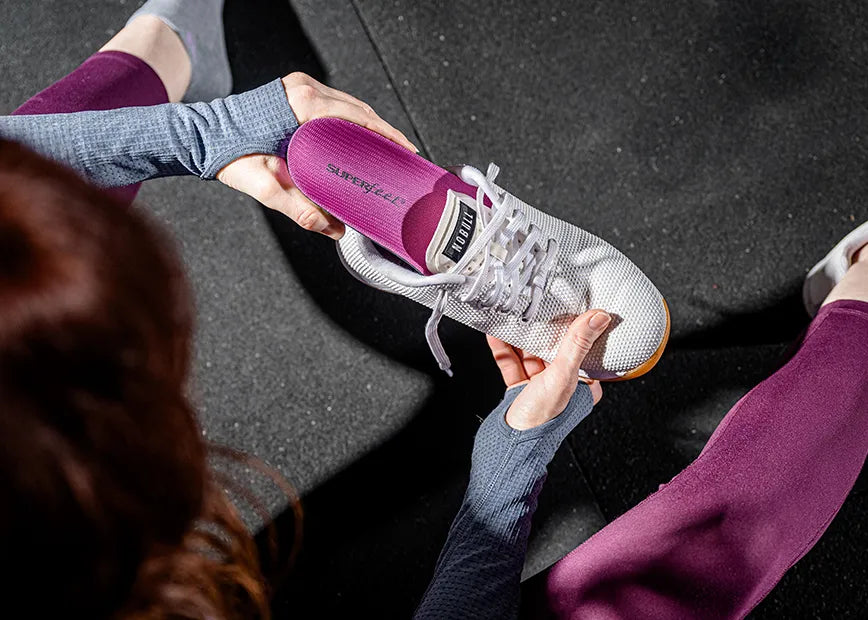 Woman in gym inserting Supferfeet High Impact Support Berry Insole into her gym shoe.