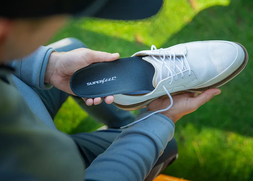 Man on golf course inserting Superfeet Casual Support insoles into his golf shoes.