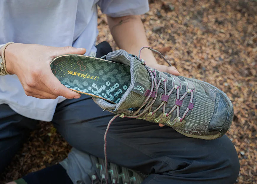 Man on a trail inserting a Superfeet Hike Cushion insole into his hiking shoe.