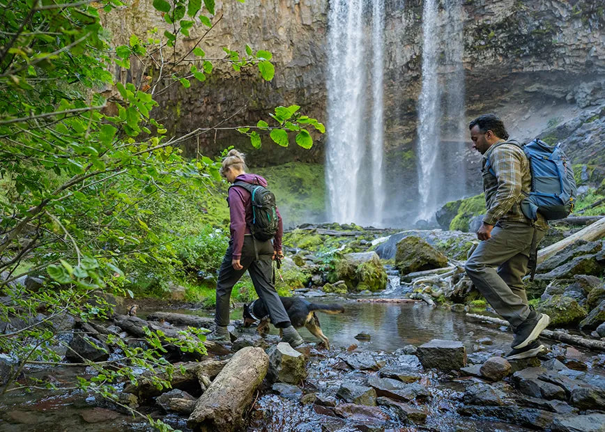 Man and woman hiking through rocky river with waterfall in background while wearing Superfeet hiking insoles.