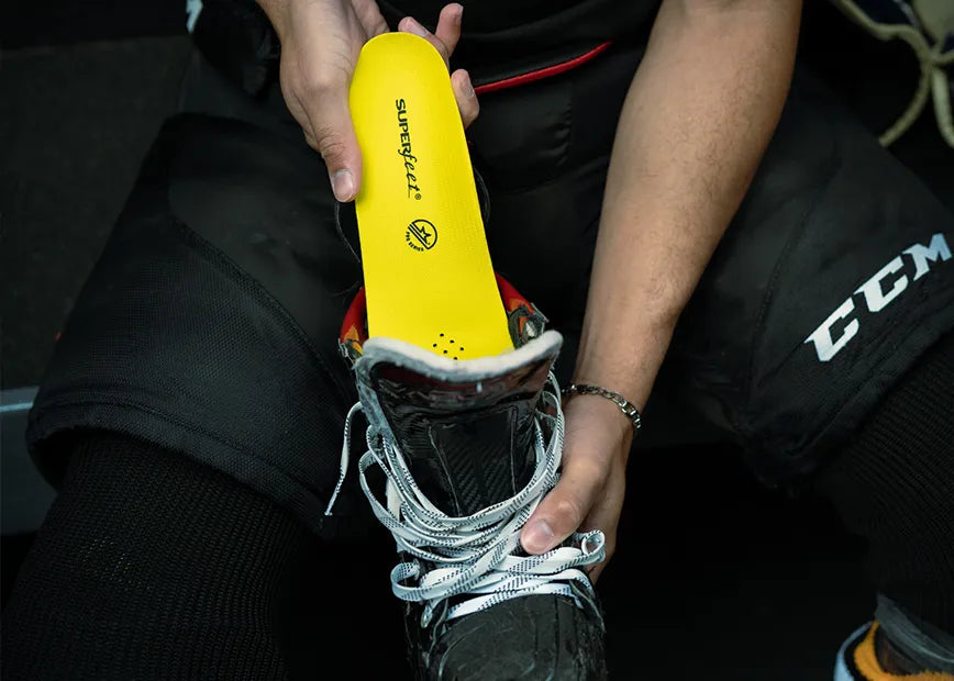 Man in hockey uniform inserting a Superfeet Hockey Performance insole into his hockey skate.