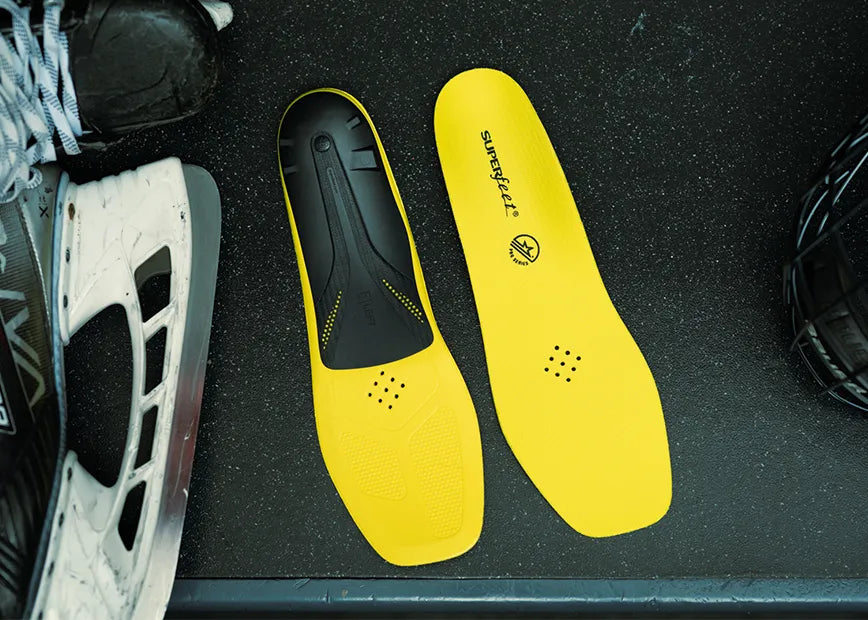 Superfeet Hockey Performance insoles on floor next to hockey skates and a hockey helmet.