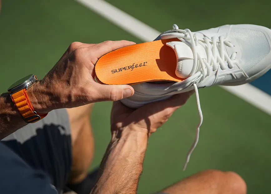 Man on pickleball court inserting a Superfeet All-Purpose High Impact Support insole into his athletic shoe.