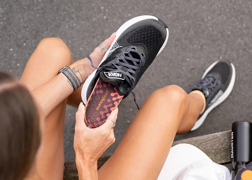 Woman getting ready for a run, inserting a Superfeet Run Cushion Low Arch insole into her running shoe.