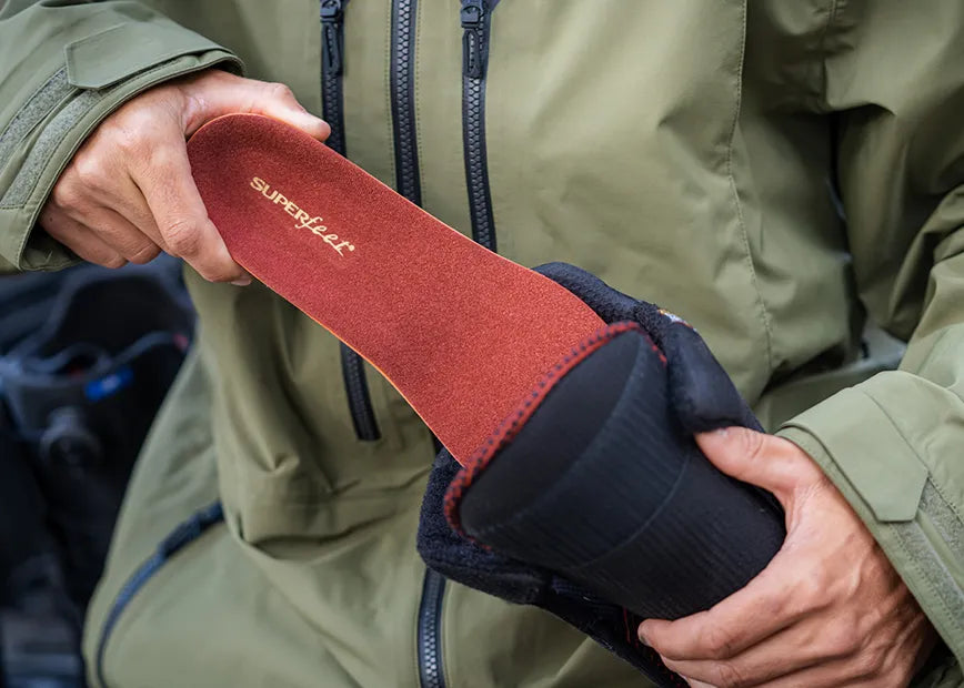 Man in outdoor gear inserting a Superfeet Winter Support insole into a snowboard boot.