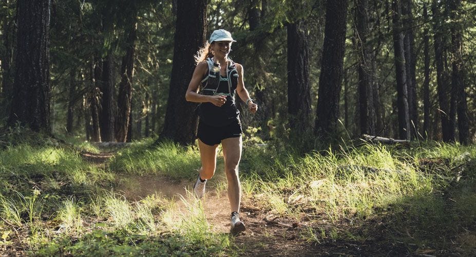 Woman runs down a dirt trail in the forest.