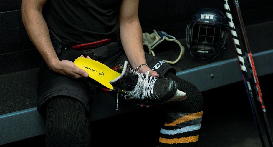 Hockey player in a locker putting a Superfeet Hockey Performance insole in his skate.